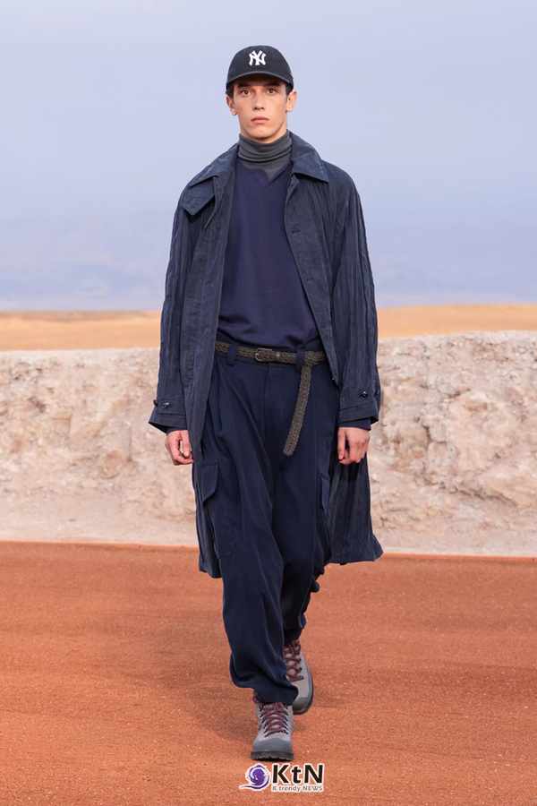 워싱 네이비 트렌치코트에 터틀넥과 주름 팬츠를 조합한 Giorgio Armani × Kith FW26 착장. 브레이디드 벨트의 긴 끝부분과 뉴욕 양키스 캡, 두툼한 신발이 부드러운 테일러링에 캐주얼한 요소를 더한다. 사진=Kith and Giorgio Armani, K trendy NEWS DB ⓒ케이 트렌디뉴스 무단전재 및 수집, 재배포금지